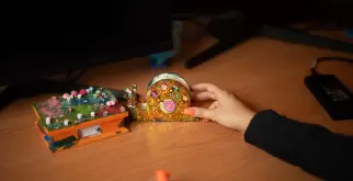Auf dem Arbeitstisch stehen ein Klebeband und ein Notizenhalter. Sie sind mit Glitzer und Steinen verziert und wurden für Saphir an einem Workshop für Kinder erstellt. 