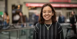 A picture of Saphir Ben Dakon, she is laughing and looking directly into the camera. She is wearing her golden glasses and a black sweater with vertical white stripes.
